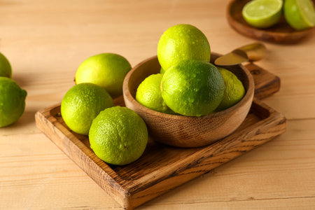 Bowl and cutting board with fresh ripe limes on wooden background, closeupの写真素材