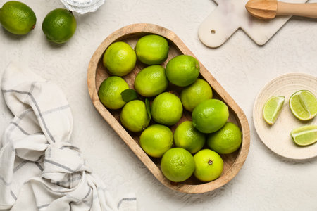 Wooden tray and plate with fresh ripe limes on white backgroundの写真素材