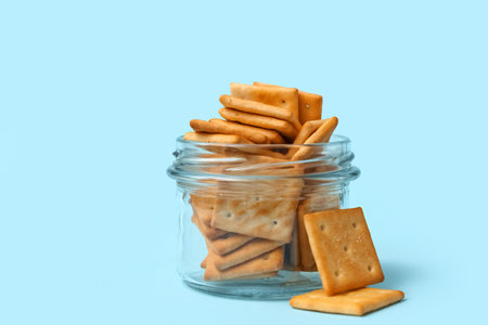 Glass jar with tasty crackers on blue background, closeupの写真素材