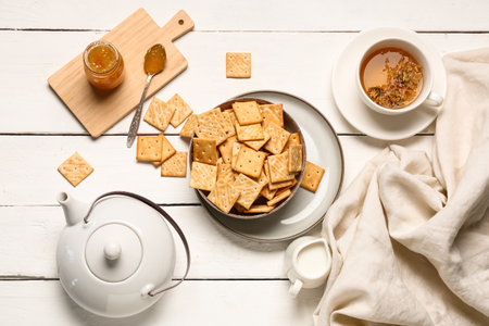 Composition with bowl of tasty crackers, teapot and cup of tea on white wooden backgroundの写真素材