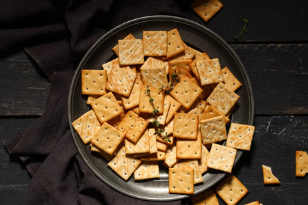 Composition with plate of tasty crackers on black wooden background, closeupの写真素材