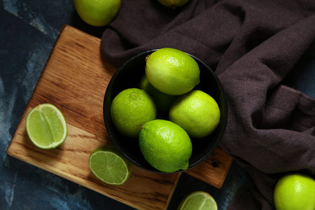 Bowl and wooden board with fresh ripe limes on blue backgroundの写真素材
