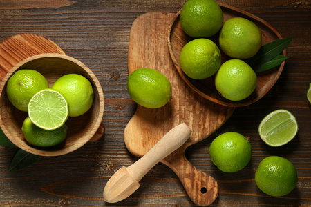 Bowl and plate with fresh ripe limes on wooden background
