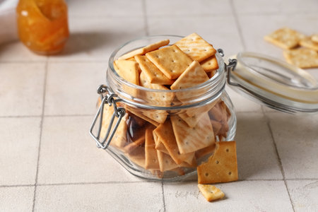 Composition with glass jar of tasty crackers on beige tile background, closeupの写真素材