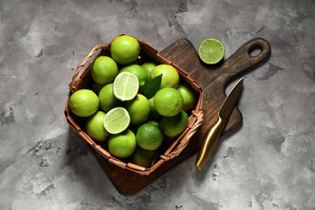 Wicker basket with fresh ripe limes on gray background