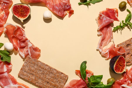 Frame made of delicious prosciutto slices, fresh fig, basil leaves, crispbread and mozzarella cheese on yellow backgroundの写真素材