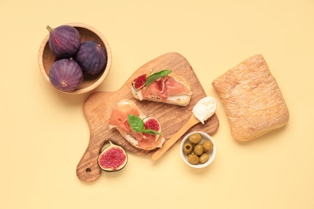 Wooden board of bread slices with delicious prosciutto and fresh fig on yellow backgroundの写真素材