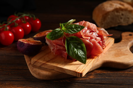 Board with delicious prosciutto slices, fig and basil leaves on wooden backgroundの写真素材