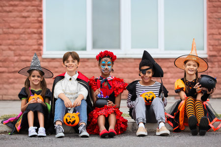 Group of kids dressed for Halloween with candies sitting on streetの写真素材