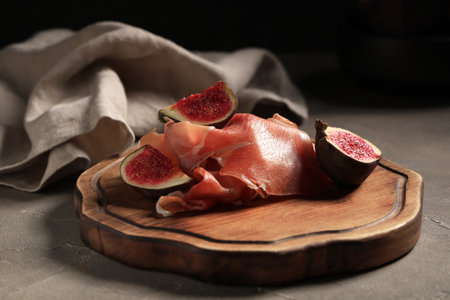 Wooden board with delicious prosciutto slices and fresh fig on gray tableの写真素材