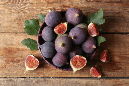 Bowl with fresh ripe figs and leaves on wooden background