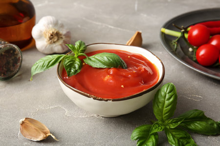 Bowl of tasty tomato sauce with basil leaves and garlic on gray background, closeupの写真素材