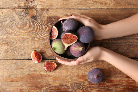 Female hands with bowl of fresh ripe figs on wooden backgroundの写真素材