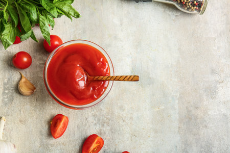 Glass bowl of tasty tomato sauce with garlic and basil leaves on gray backgroundの写真素材