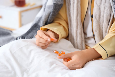 Ill young woman taking throat lozenges in bedroom, closeupの写真素材
