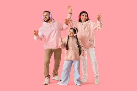 Happy parents with their little daughter in headphones dancing on pink backgroundの写真素材