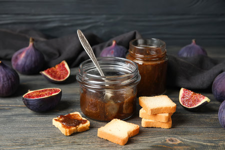 Jars of sweet fig jam and tasty toasts on black wooden table, closeupの写真素材