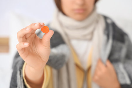 Ill young woman with throat lozenge in bedroom, closeupの写真素材