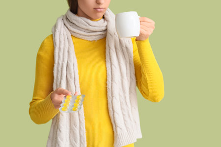 Young woman with throat lozenges and cup of tea on green backgroundの写真素材