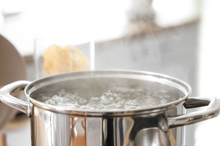 Stainless steel pot with boiling water on stove in kitchen, closeup