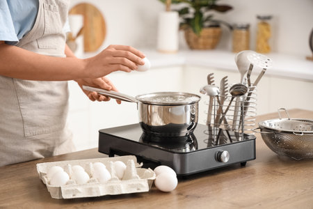 Woman putting egg into saucepan with boiling water in kitchenの写真素材