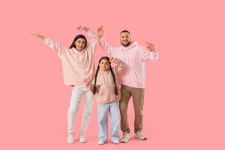 Happy parents with their little daughter dancing on pink backgroundの写真素材