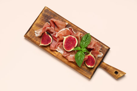 Wooden board with prosciutto slices, fresh fig and basil leaves on beige backgroundの写真素材