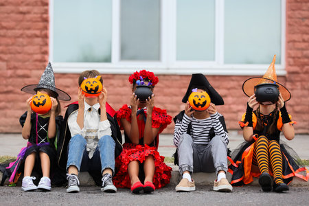 Group of kids dressed for Halloween with candies sitting on streetの写真素材