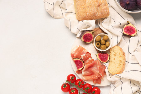 Board with prosciutto slices, fresh figs, ciabatta and cherry tomatoes on white backgroundの写真素材