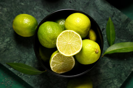 Bowl with fresh ripe limes and leaves on green backgroundの写真素材