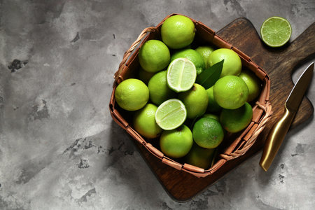 Wicker basket with fresh ripe limes on gray background