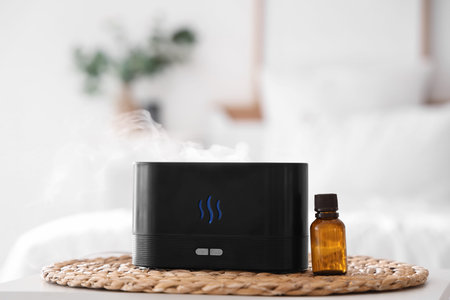 Air humidifier with essential oil on table in bedroom, closeup
