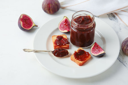 Plate with jar of sweet fig jam and tasty toasts on marble backgroundの写真素材