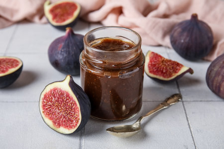Jar of sweet fig jam with spoon on white tile backgroundの写真素材