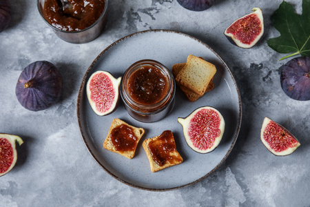 Plate with jar of sweet fig jam and tasty toasts on gray grunge backgroundの写真素材