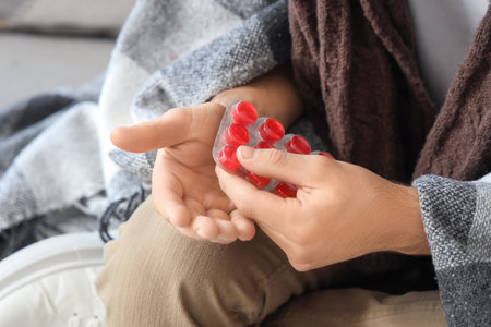 Ill young man taking throat lozenges on sofa at home, closeupの写真素材