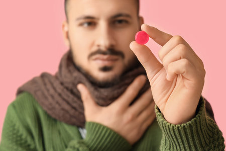 Ill young man with throat lozenge on pink background, closeupの写真素材