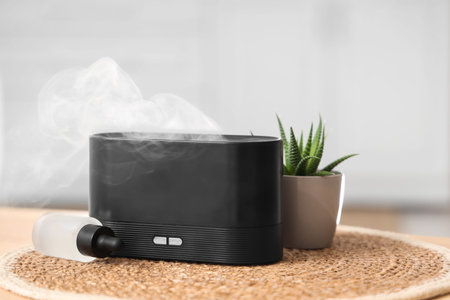 Air humidifier with essential oil and plant on table in bathroom, closeup