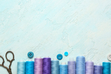 Colorful thread pools with scissors and buttons on light blue background