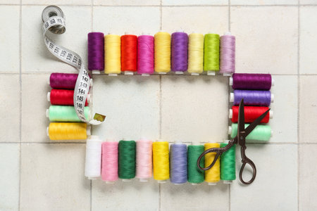 Frame made of colorful thread pools with scissors and measuring tape on white tile backgroundの写真素材