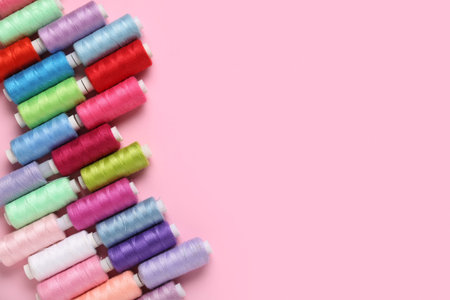Colorful thread spools on pink background