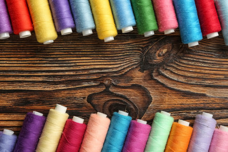 Frame made of colorful thread spools on wooden background