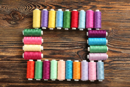 Frame made of colorful thread spools on wooden background