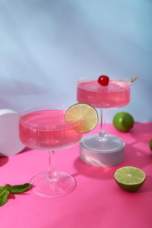 Glasses of tasty Cosmopolitan cocktail with limes and mint on pink table against blue backgroundの写真素材