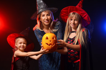 Happy girls with their grandmother dressed as witches for Halloween and pumpkin on dark backgroundの写真素材