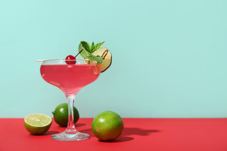 Glass of tasty Cosmopolitan cocktail garnished with cherry and mint on red table against turquoise backgroundの写真素材
