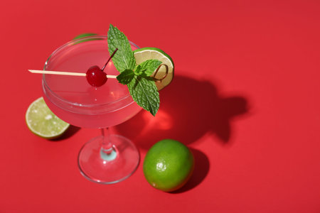 Glass of tasty Cosmopolitan cocktail garnished with cherry and mint on red background