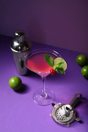 Glass of tasty Cosmopolitan cocktail garnished with cherry and lime on purple backgroundの写真素材