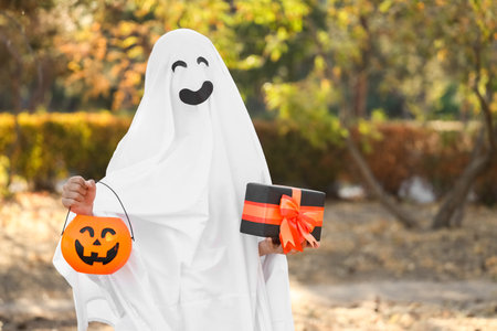 Teenage boy dressed as ghost for Halloween with gift in parkの写真素材