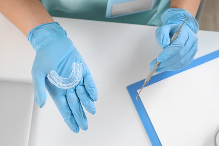 Female dentist with occlusal splint and tool at table in clinic, top viewの写真素材